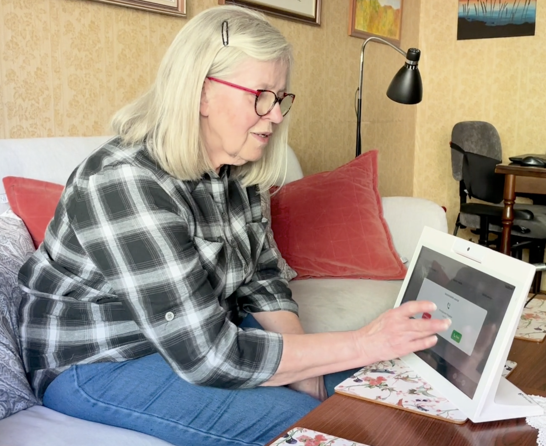 En kvinna sitter i en soffa framför en Bubblan-skärm i sitt vardagsrum och svarar på ett videosamtal.